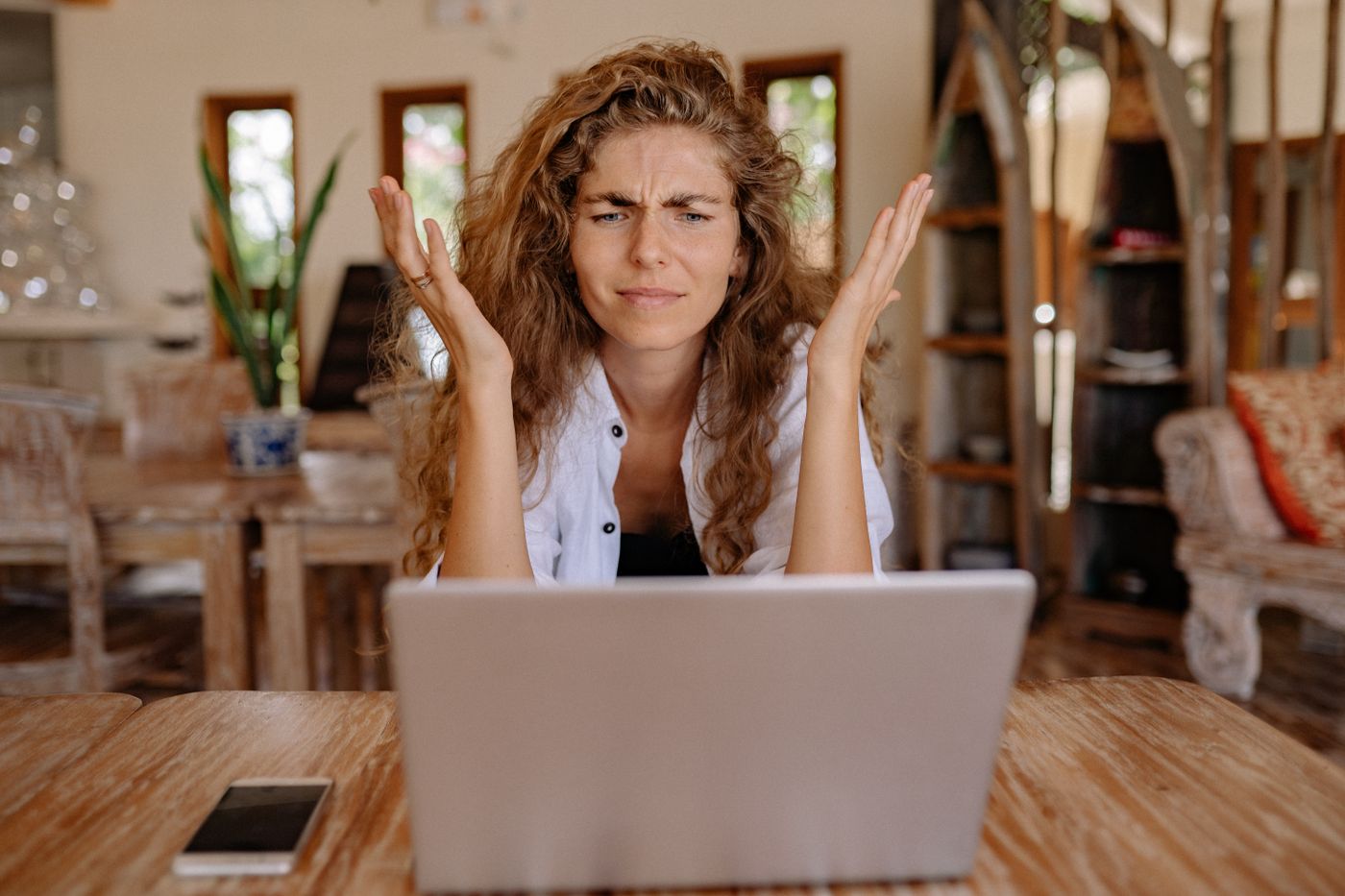A woman at a laptop throwing up her hands in exasperation at whatever has just appeared on screen